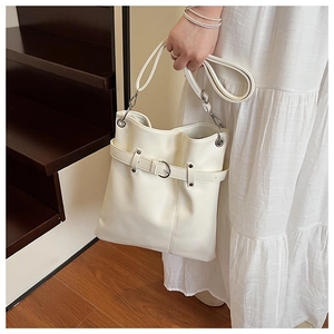 Detail of a creamy white bucket bag with a silver buckle and adjustable shoulder strap