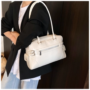 Detail view of a cream bowling bag with silver hardware on a model's shoulder