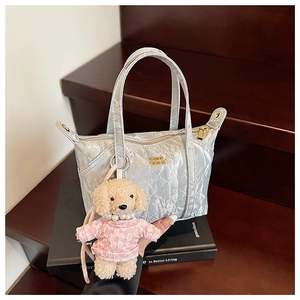 Détail du sac cabas plissé argenté avec logo doré et pendentif de chien en peluche