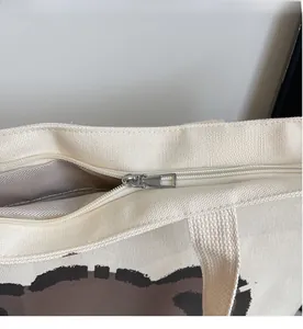 Close-up of a smooth silver metal zipper on a beige canvas tote bag with inner lining