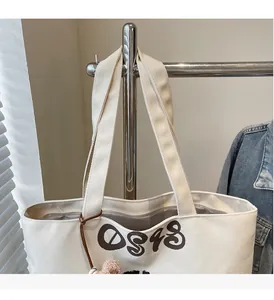Detailed shot of white canvas tote bag with DS48 print and brown plush charm