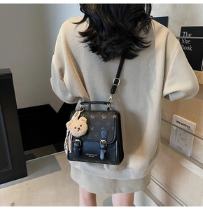 Détail du sac à dos noir imprimé avec boucle en cuir et breloque ours en peluche brun