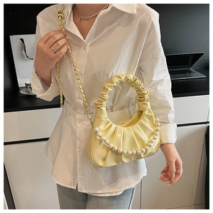 Detail of yellow pleated cloud bag with pearl chain and gold strap worn by a model