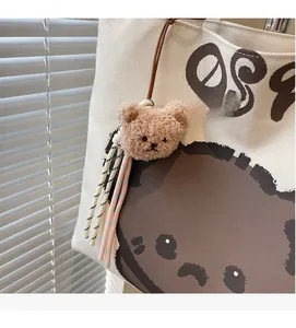 Detailed close-up of a plush bear charm with striped woven tassels on a canvas tote bag