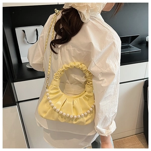 Detail view of yellow ruched cloud bag with pearl handle and golden chain strap