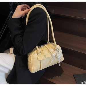 Détail d'un sac hobo en cuir crème avec pendentif nœud perlé et poche à bordure ondulée