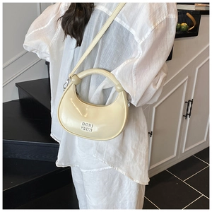 Close-up of cream crescent bag with glossy leather texture and round integrated handle