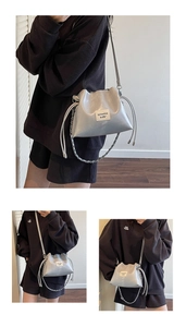 Detail of silver metallic drawstring bucket bag with adjustable straps and chain accessory