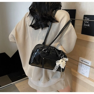 Détail d'un sac à bandoulière en cuir verni noir avec pendentif nœud en dentelle et perles