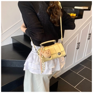 Detail of light yellow croc-effect messenger bag with cute bear charm and woven tassel
