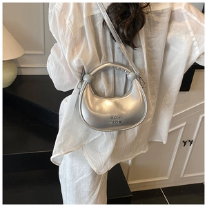 Detail view of metallic silver crescent bag with circular handle and brand logo lettering