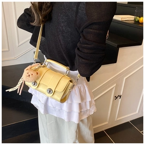 Detail of yellow crocodile embossed messenger bag with silver lock and plush bear charm