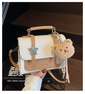 Detailed close-up of a two-tone crossbody bag with silver star buckle and plush bear charm