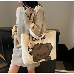 Detail of canvas tote bag featuring a brown cartoon bear print and plush bear charm accessory