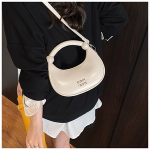 Creamy white crescent bag worn crossbody, showing smooth glossy finish and metal lettering