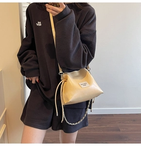 Detail of beige drawstring shell bag with metal chain strap worn by a stylish model