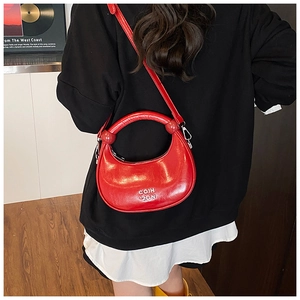 Detail of bright red patent leather crescent bag with hard arc handle and shoulder strap