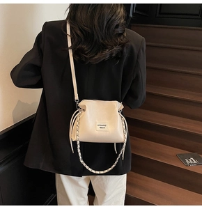 Detail of cream white bucket bag with drawstring closure and stylish leather chain strap