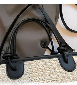 Dettaglio della borsa tote in paglia intrecciata con manici in ecopelle nera e nodi decorativi