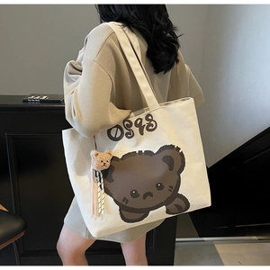 Detailed view of beige canvas tote bag with cute bear print and plush bear charm accessory