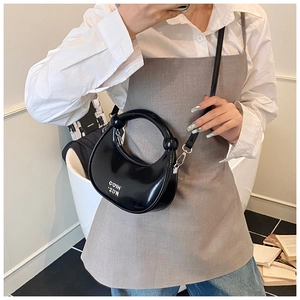 Close-up of black patent leather crescent bag with decorative knot handle and metal hooks