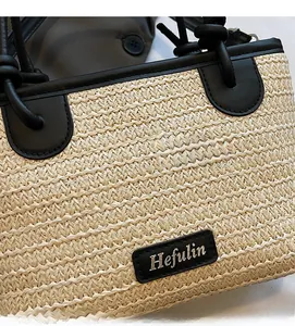 Dettaglio ravvicinato della borsa in paglia intrecciata con finiture in pelle nera e logo argento