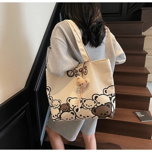 Close-up of canvas tote bag featuring cute cartoon bear prints and a plush bear pendant