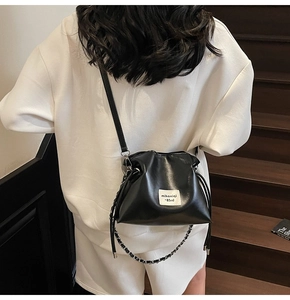 Detail of a black drawstring bucket bag featuring a white logo label and metal chain strap