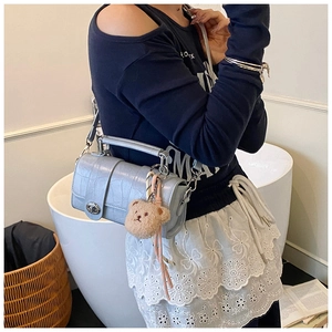 Detail of light blue croc-embossed messenger bag with metal turn-lock and bear charm