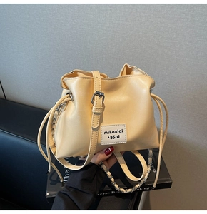 Detail shot of a cream-colored bucket bag with drawstring and adjustable metal chain strap