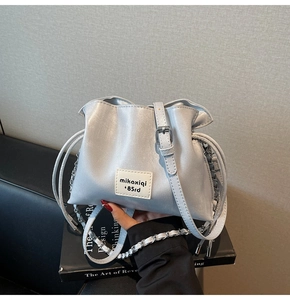 Detail of silver shell bag with drawstring closure, leather strap and metal chain handle