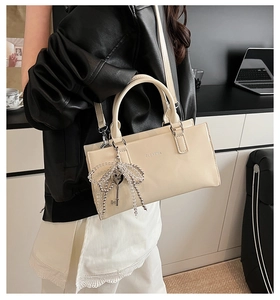 Detail of cream shoulder bag with pearl bow charm and adjustable strap for women