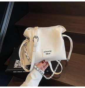 Detail view of cream shell bag with drawstring closure and silver chain strap