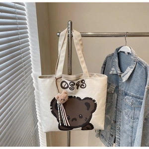 Close-up of cream canvas tote bag with bear print and cute plush bear keychain