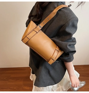Vue détaillée du sac cylindrique marron avec bandoulière réglable sur blazer gris