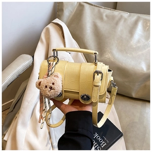 Detail of yellow crocodile embossed messenger bag with cute brown plush bear charm