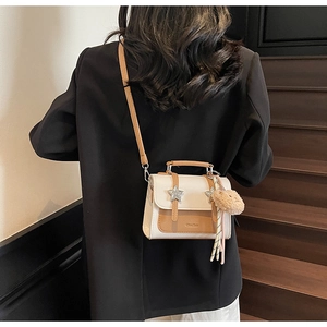 Detail of a white and tan crossbody bag with star accents and plush charm on a model