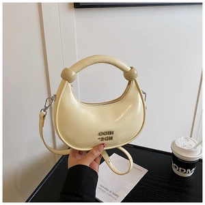 Detailed shot of cream crescent bag with glossy finish and silver letter hardware logo