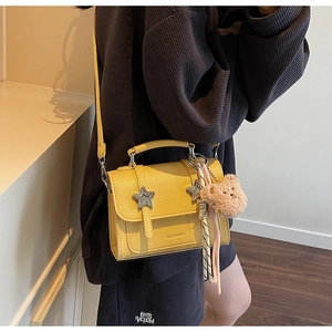 Detail view of yellow lychee leather bag with star buckles and bear charm on model