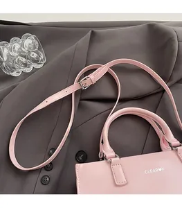 Detail view of pink leather handbag with brand logo, top handles and adjustable strap