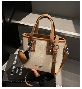 Close-up of cream and brown leather bucket bag with silver rivets and heart charm