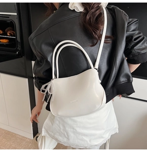 Détail du sac seau en cuir blanc avec pendentif nœud en perles et logo GILARUX