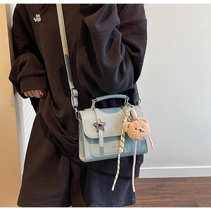 Detail of light blue lychee pattern handbag featuring a star buckle and teddy bear charm