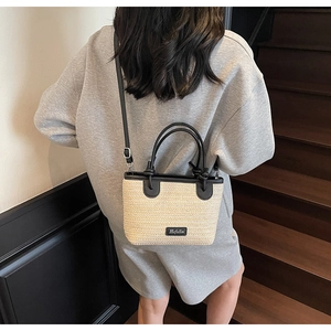 Dettaglio della borsa in paglia intrecciata con finiture in pelle nera e logo Hefulin