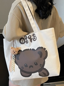 Canvas tote bag with cartoon bear print and plush charm shown in a lifestyle view