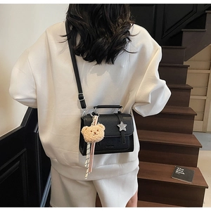 Detail view of black pebble leather crossbody bag with star decor and plush bear charm