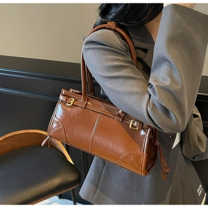 Brown glossy leather shoulder bag shown on model with side buckle and drawstring detail