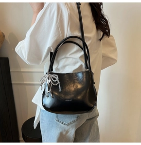 Détail du sac seau noir en demi-lune avec nœud perlé argenté et pendentif en clé