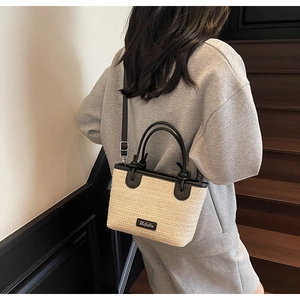 Dettaglio di una borsa a secchiello in paglia beige con tracolla in pelle nera su scale