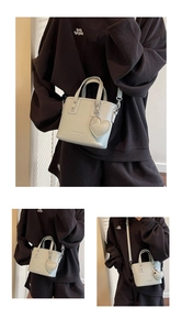 Detail of cream bucket bag with lychee texture, heart charm, and metallic strap hooks